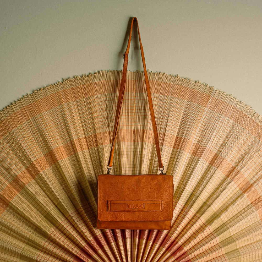 Tan leather knitting needle and crochet hook case hanging on a decorative wall fan against a light green wall.