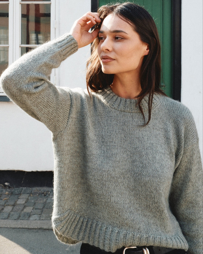 A woman wearing the Knitting for Olive Astrid Sweater, showing the dropped shoulder and curved ribbed hem