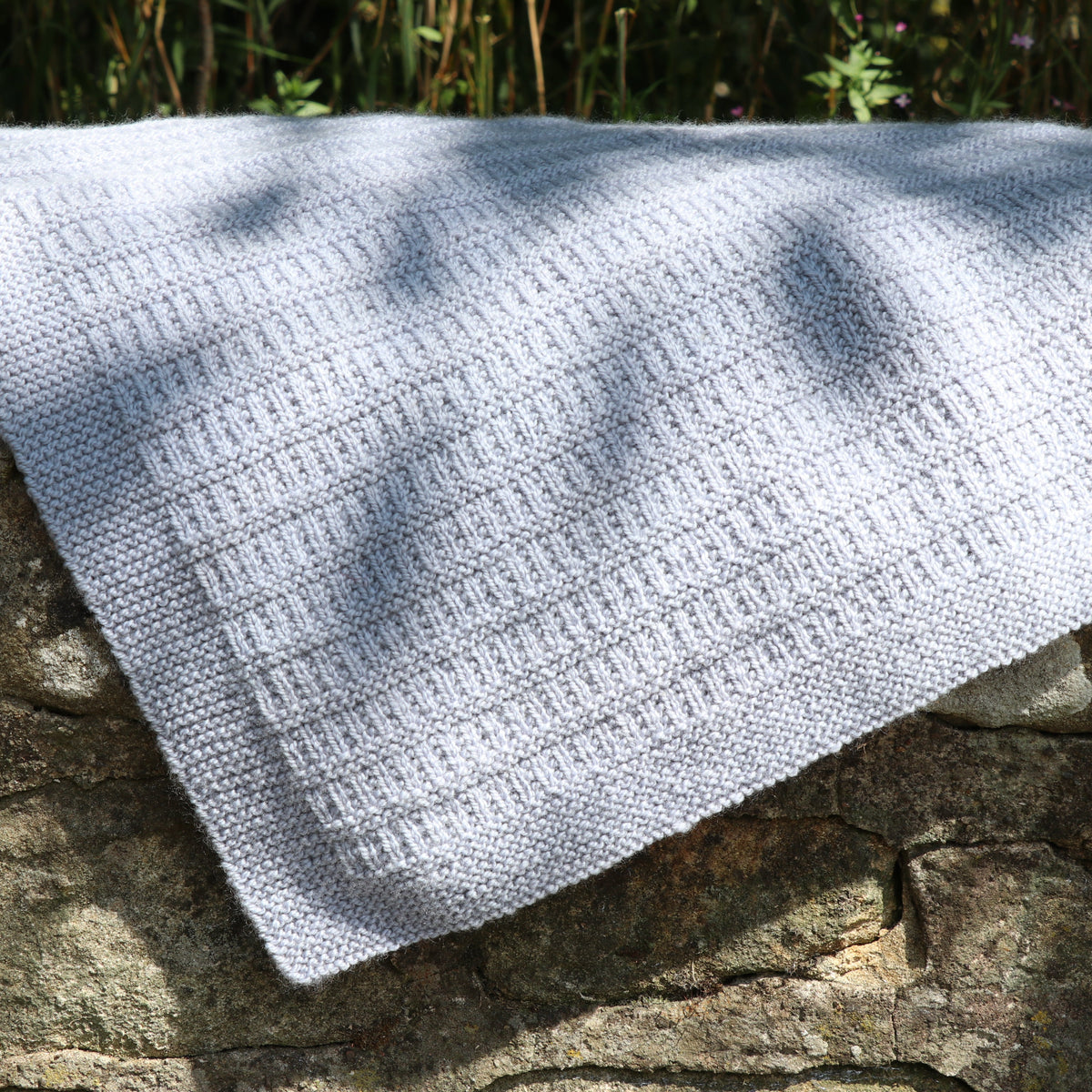 The Cassilis Baby Blanket draped over moss-covered rock, showing its drape and softness