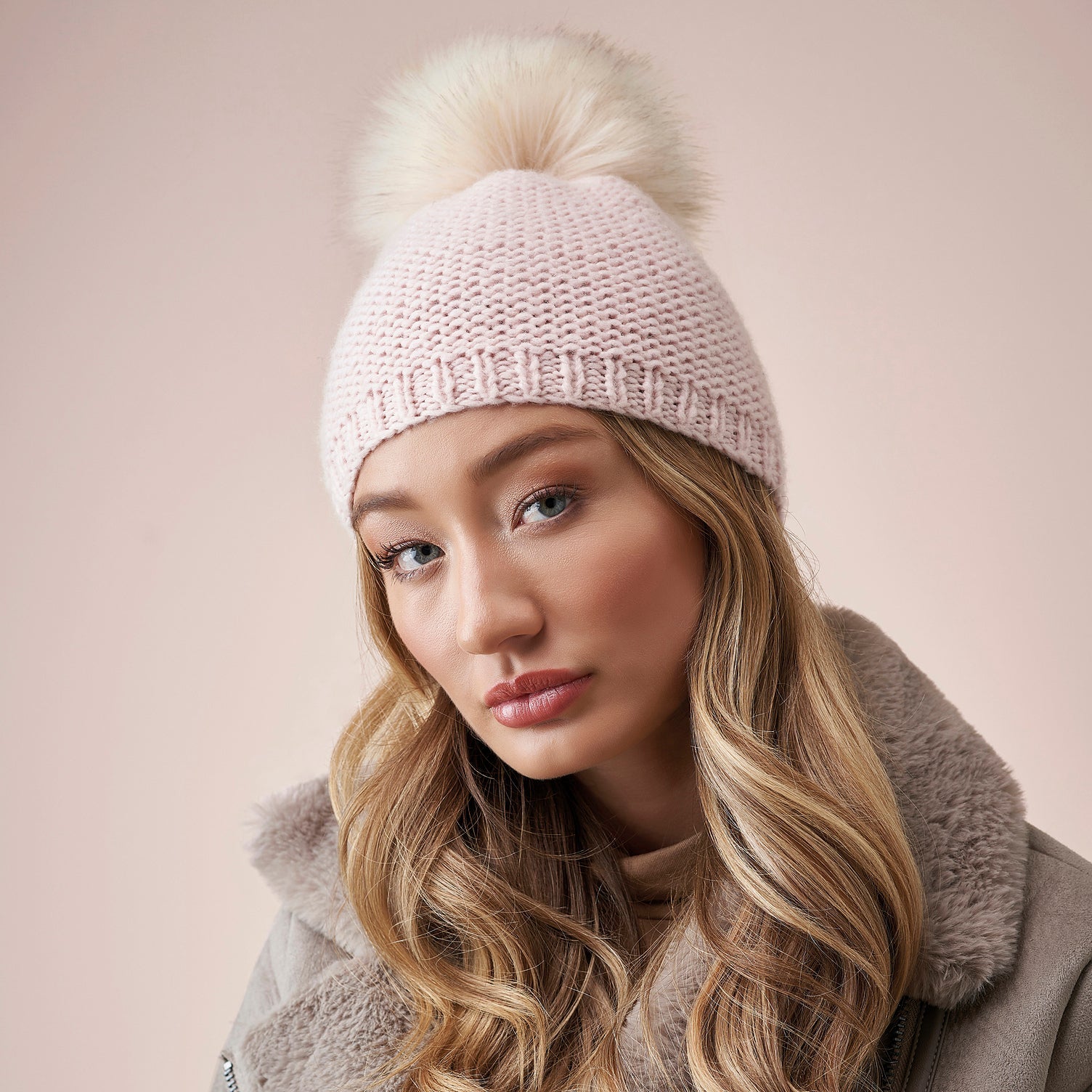Woman wearing a pink knit beanie with a pom-pom on a beige background