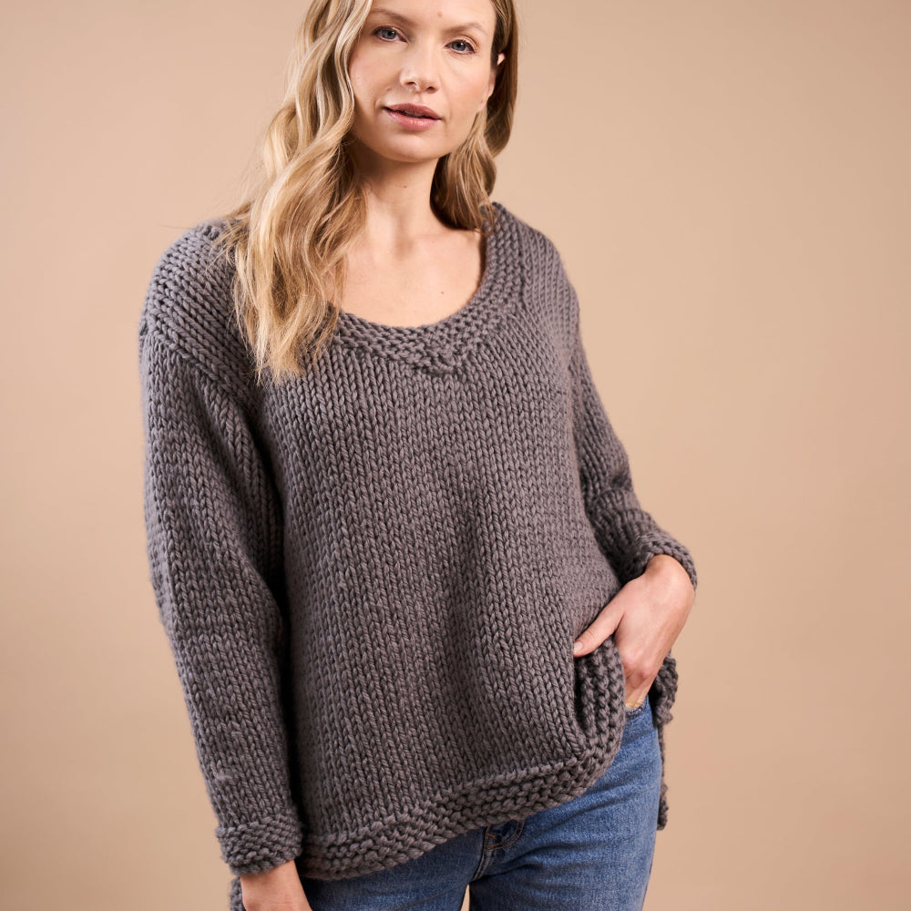 Woman wearing a chunky knit sweater and jeans against a beige background