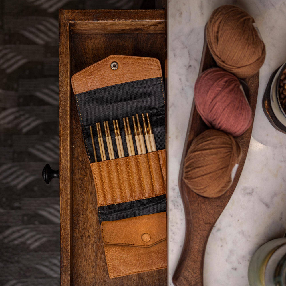 A foldable leather case with compartments, displayed alongside knitting needles and yarn, suggesting its use for storing and organizing knitting supplies.